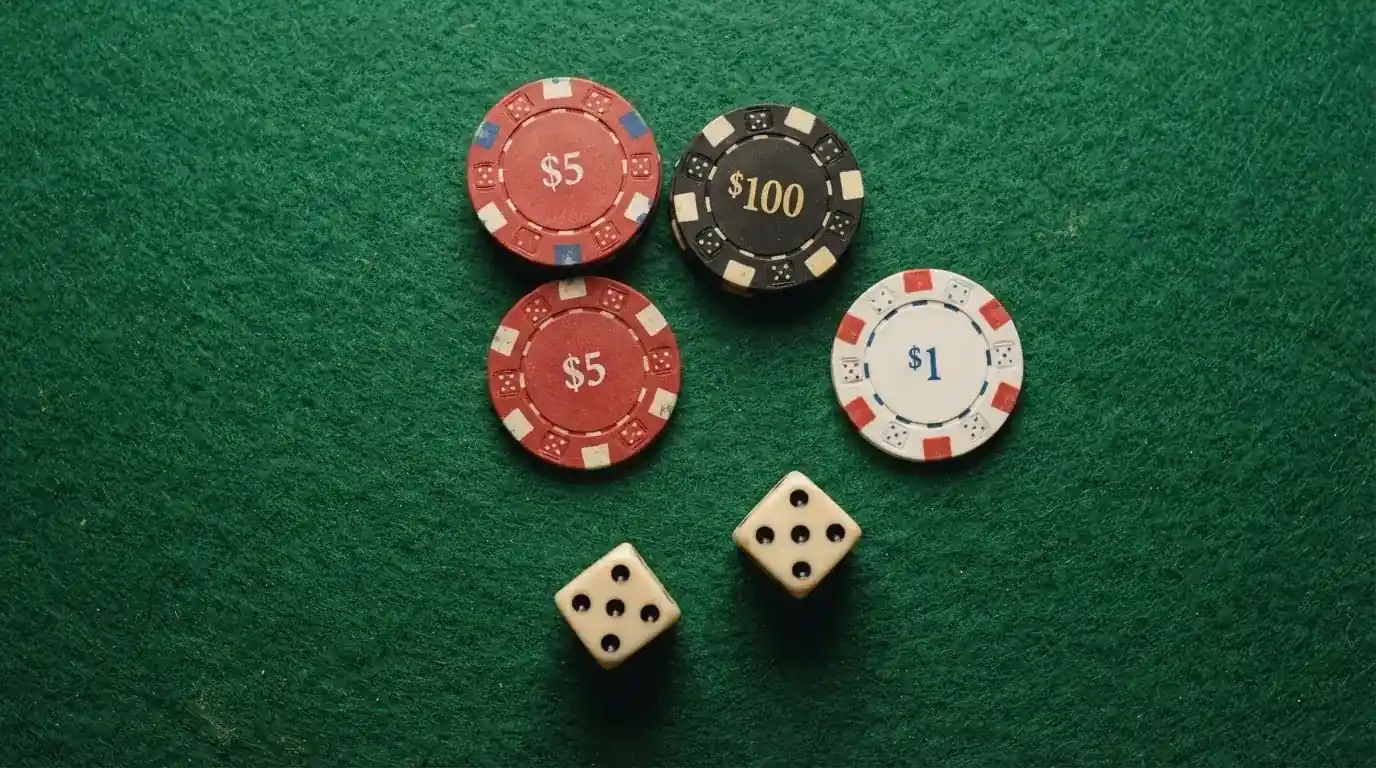 Vista cenital de fichas de casino y dados sobre una mesa de fieltro verde bajo luz suave.