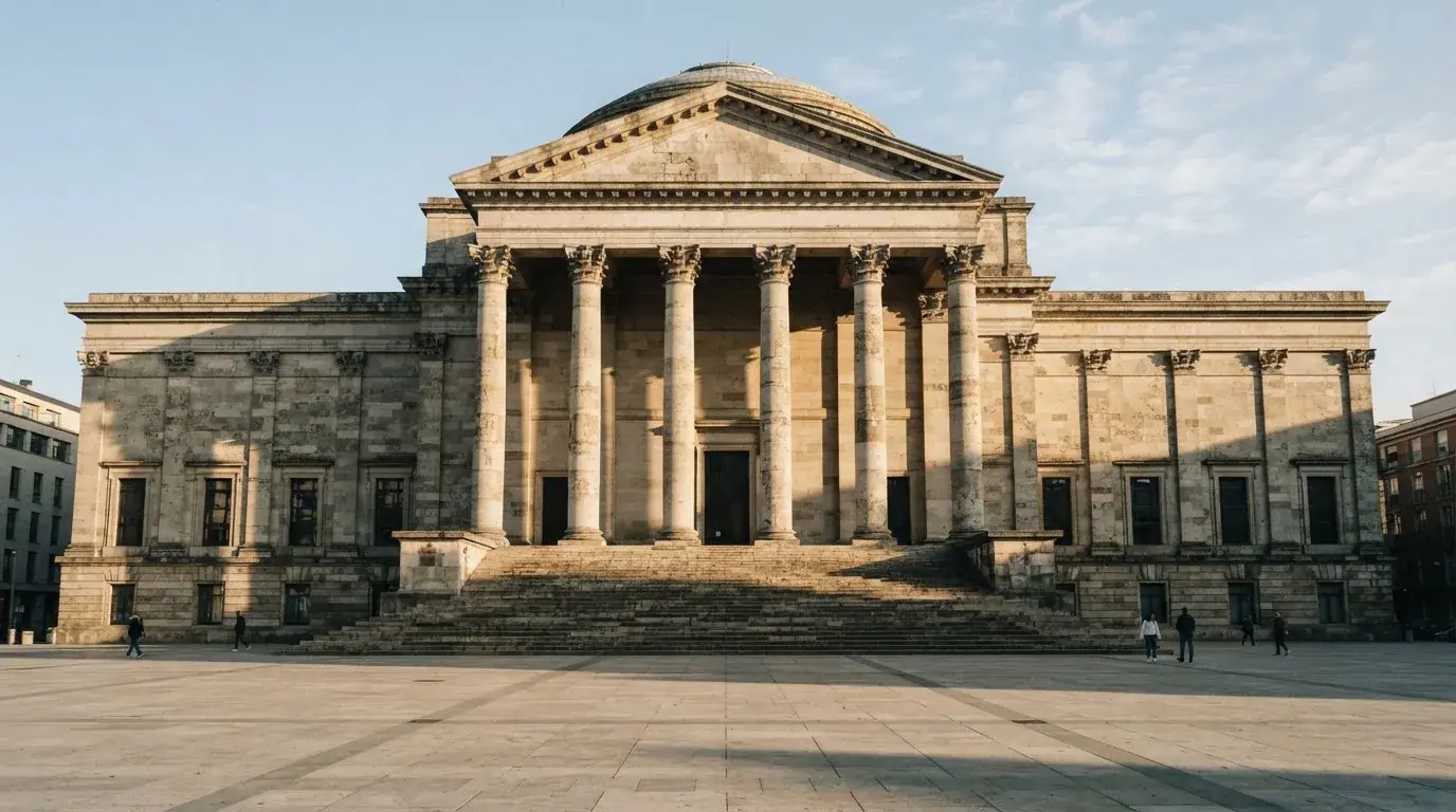 Un edificio institucional de piedra con columnas clásicas bajo un cielo despejado en una plaza amplia.